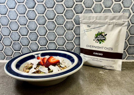 Bowl of cacao overnight oats with strawberries next to a package of Dr. Mak's Superfoods on a tiled countertop.